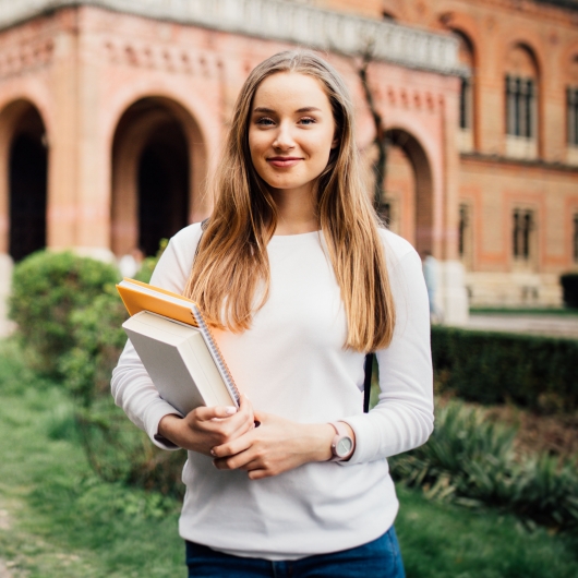 Female student on college campus with books in arms