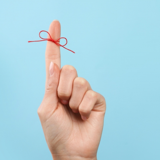 Finger with red string tied around it in front of blue background